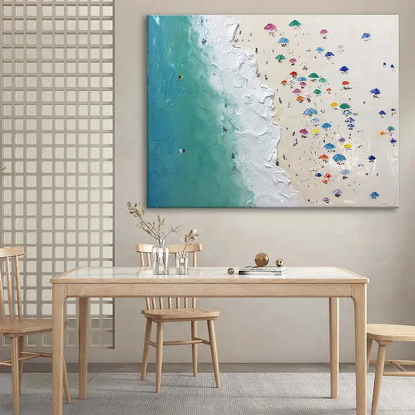A large horizontal wall art of blue sea waves splashing onto the beige beach dotted with colorful umbrellas. 
