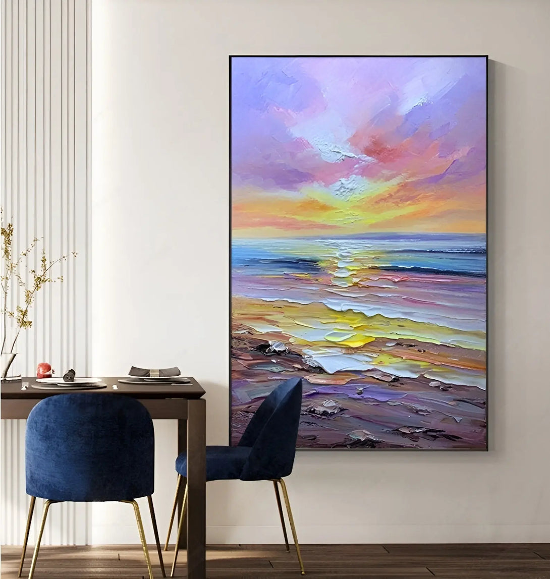 A large vertical textured wall painting of purple textured beach with blue ocean, bathed in the yellow sunlight beneath the purple sky. 