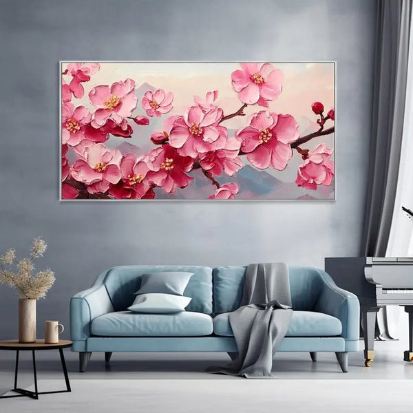 A large horizontal plaster wall art featuring a delicate branch of pink cherry blossoms, set against a breathtaking backdrop of rolling mountain ranges shrouded in mist.
