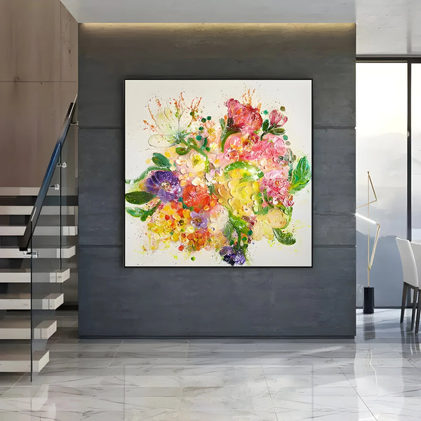 A large square painting of flowers in pink, yellow and purple with green leaves against a white backdrop. 