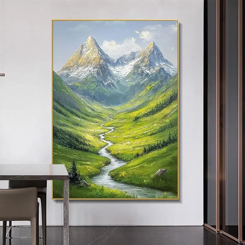 A large textured wall art of a narrow stream flowing in between green rolling hills, leading to snowy peaks in the background. 