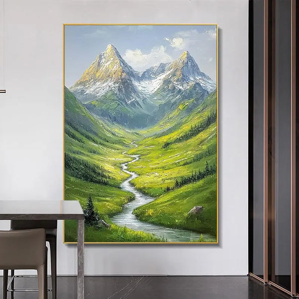 A large textured wall art of a narrow stream flowing in between green rolling hills, leading to snowy peaks in the background. 