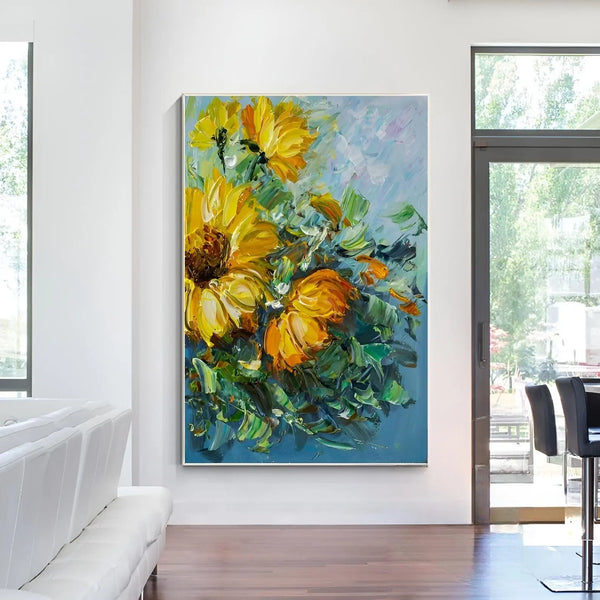 A large vertical textured wall art of 4 yellow and orange sunflowers with green leaves against a blue backdrop
