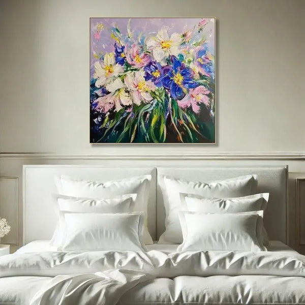 A square abstract flower painting with textured layers of purple, blue, cream, pink, and yellow petals surrounded by green foliage on a scenic canvas background.