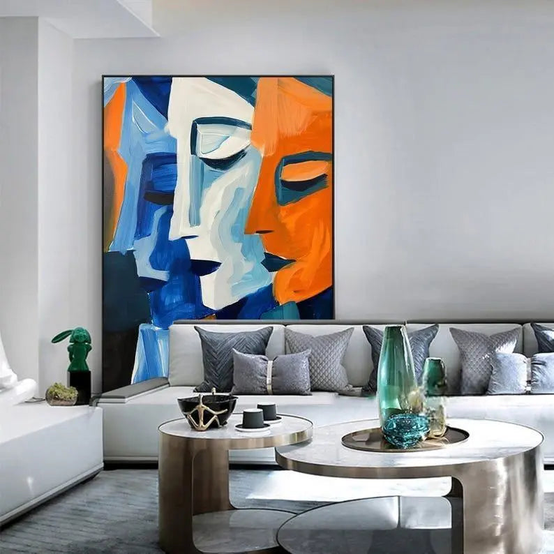 A vertical textured wall art featuring 3 human face profiles, one in dark blue, one in light blue, and another in orange. 