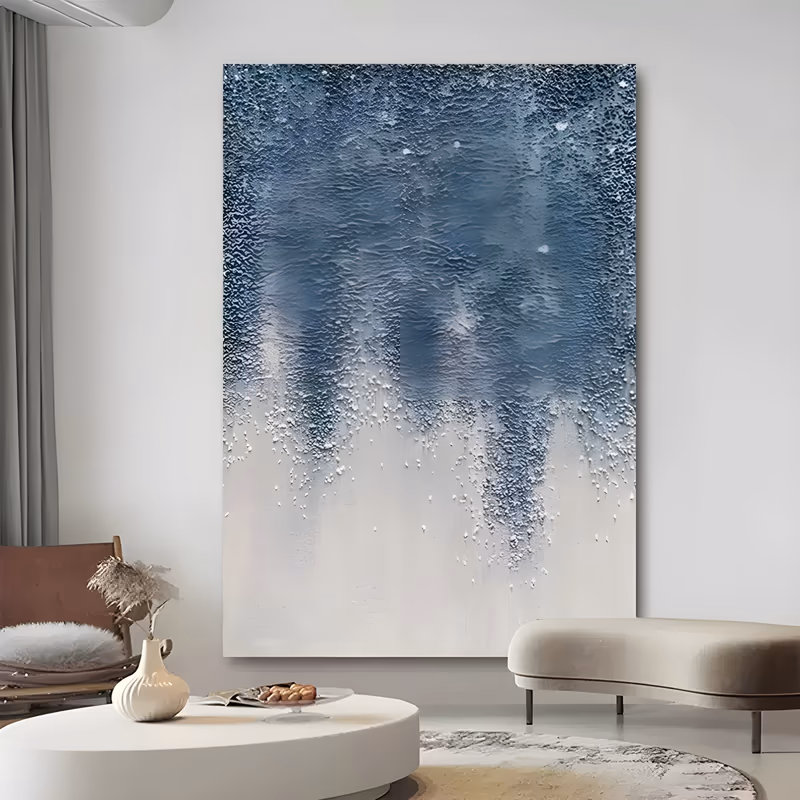 a large vertical abstract painting of a coarse granular blue field filling the upper canvas and breaking into drips and flecks as it meets a smooth white lower half, in gritty sand texture