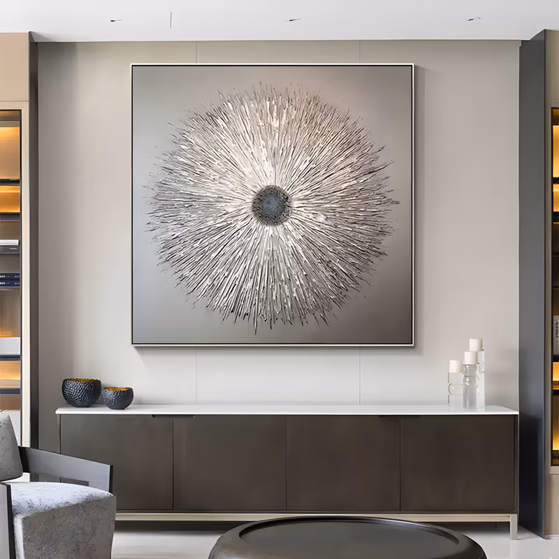 a large square textured painting of a silver-gray starburst radiating from a small dark charcoal core to the canvas corners, built up in thick sculpted plaster ridges over a soft graduated gray ground