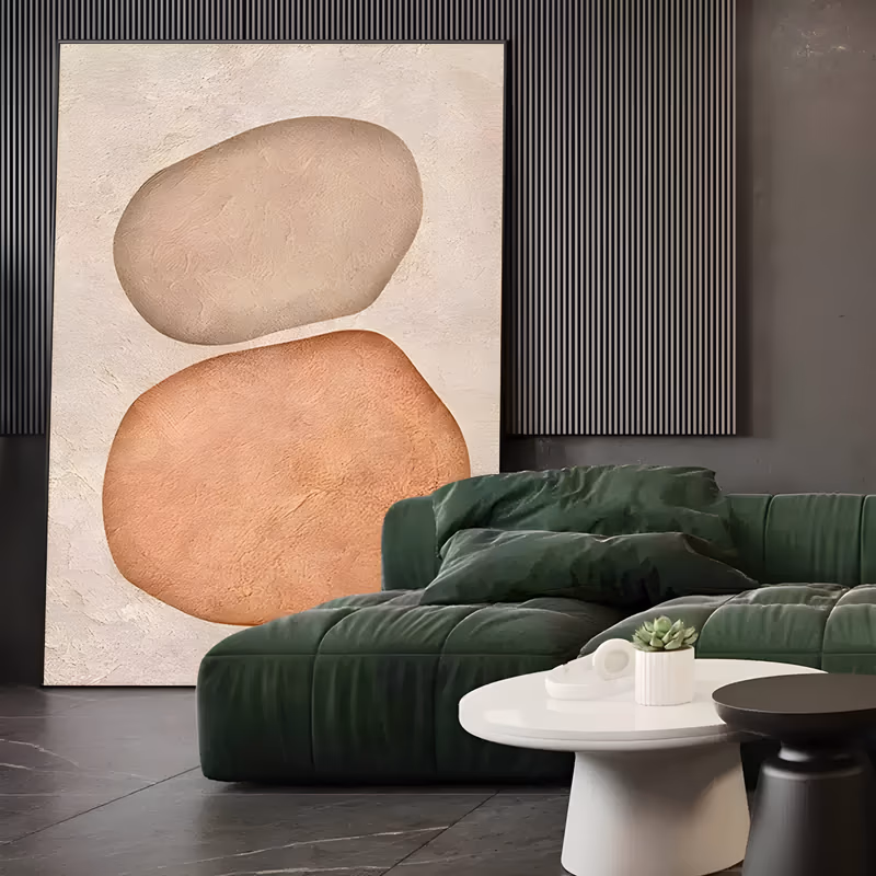 a large vertical textured painting of two stacked pebble forms, a taupe oval resting on a bigger terracotta stone, modeled in heavy raised plaster relief on a cream ground with a rough sculpted surface