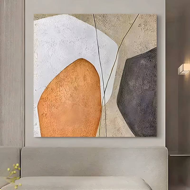 a large square wabi-sabi painting of three rounded pebble forms, a white one at top left, a terracotta one below it and a dark gray one at right, on a beige ground cut by two fine dark lines, in thick plaster relief