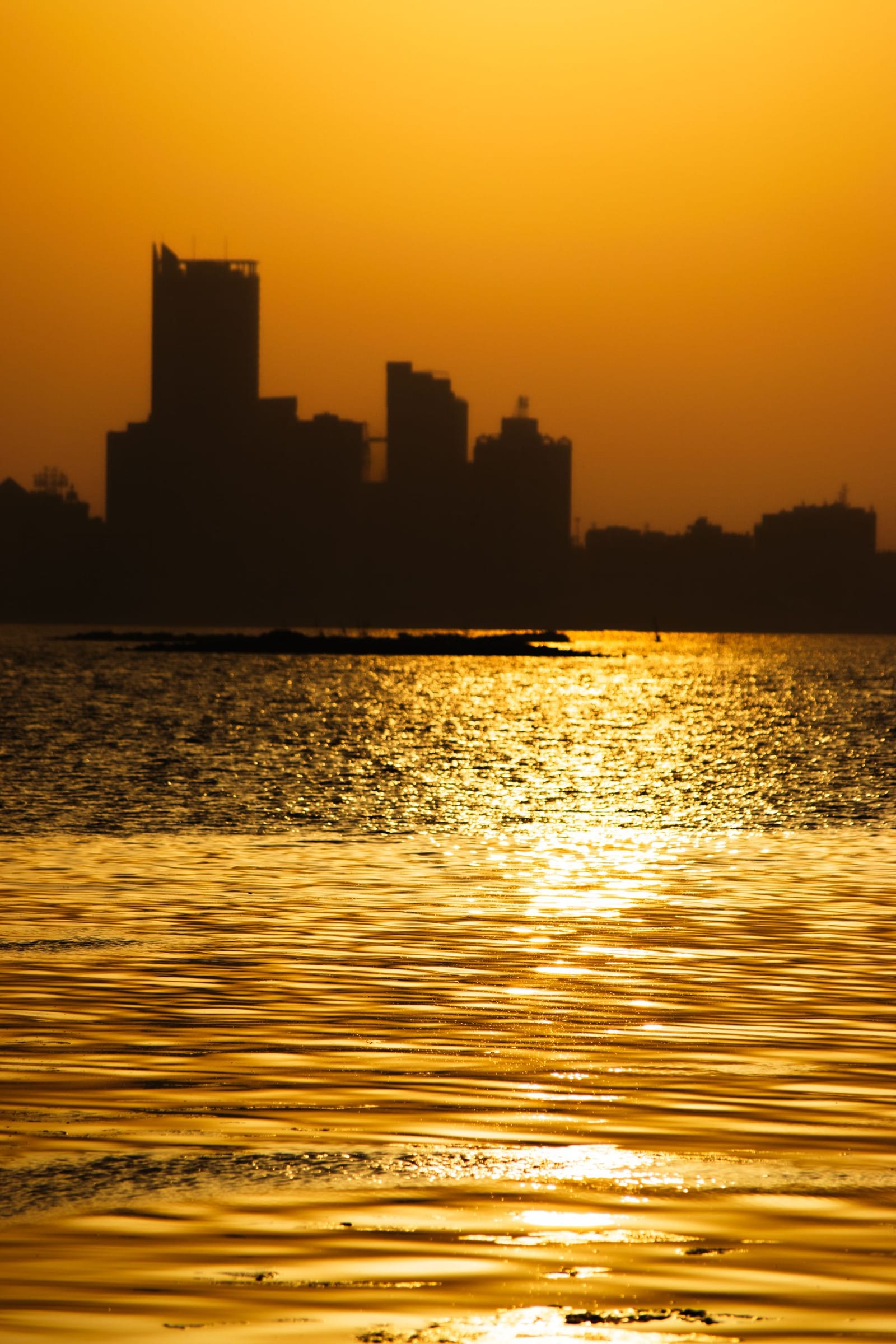 The Manama skyline in silhouette against an orange and violet sunset over the Gulf.