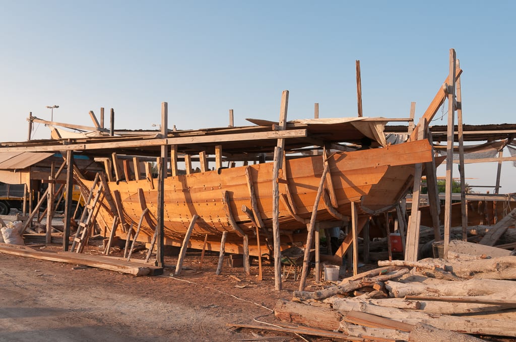 A wooden dhow under construction in the Muharraq shipyard, its hull planking exposed.
