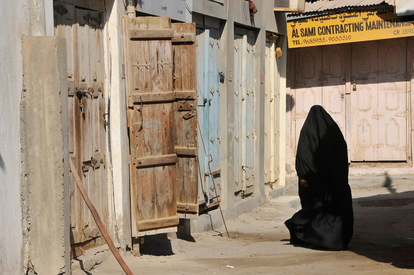 A shaded lane of the Muharraq souq with small shops and hanging goods on either side.