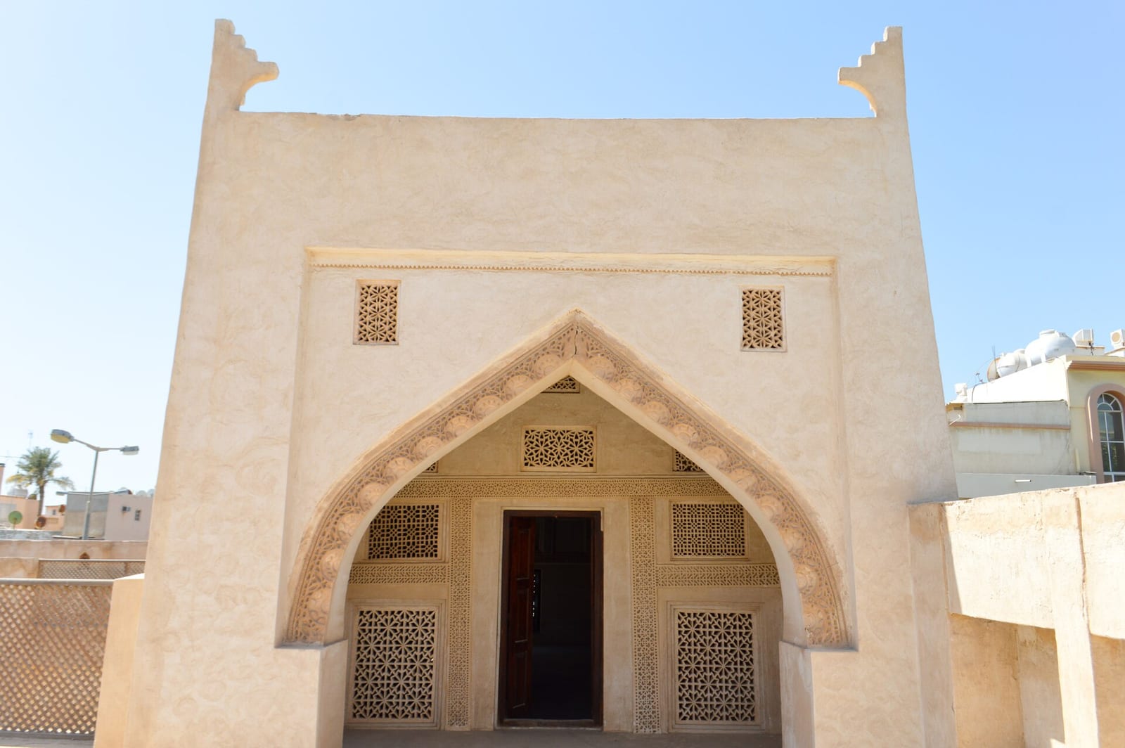 The pointed-arch entrance of Shaikh Isa bin Ali House in Muharraq, framed by carved gypsum lattice screens in pale sand-coloured plaster.