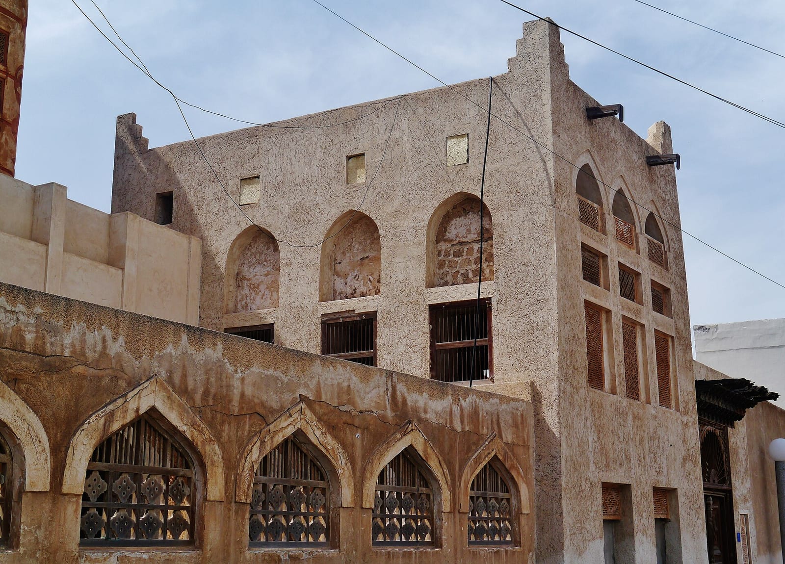 The weathered coral-stone façade of Siyadi House in Muharraq with pointed arches, lattice windows and a stepped parapet.