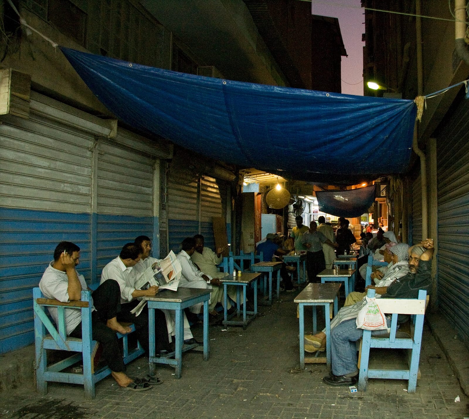A street café with plastic chairs and shaded tables in the lanes of central Manama souq.