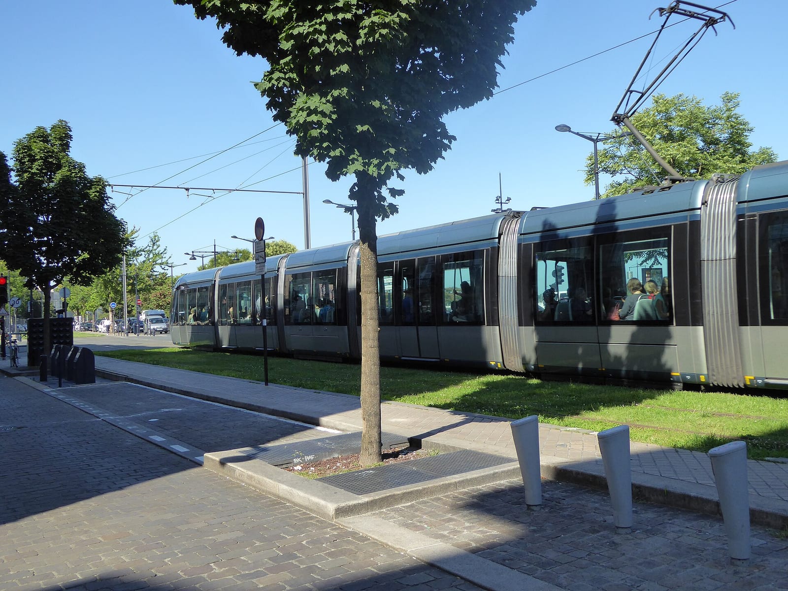 A tram passing along the tree-lined Quai des Chartrons in Bordeaux with the river on one side.
