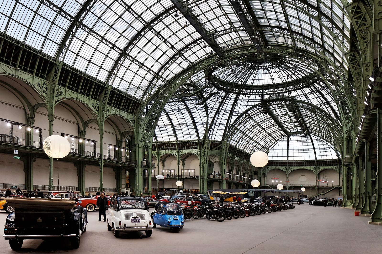 The glass-and-iron nave of the Grand Palais in Paris set up for an auction, with lots lined up on the floor under the roof.