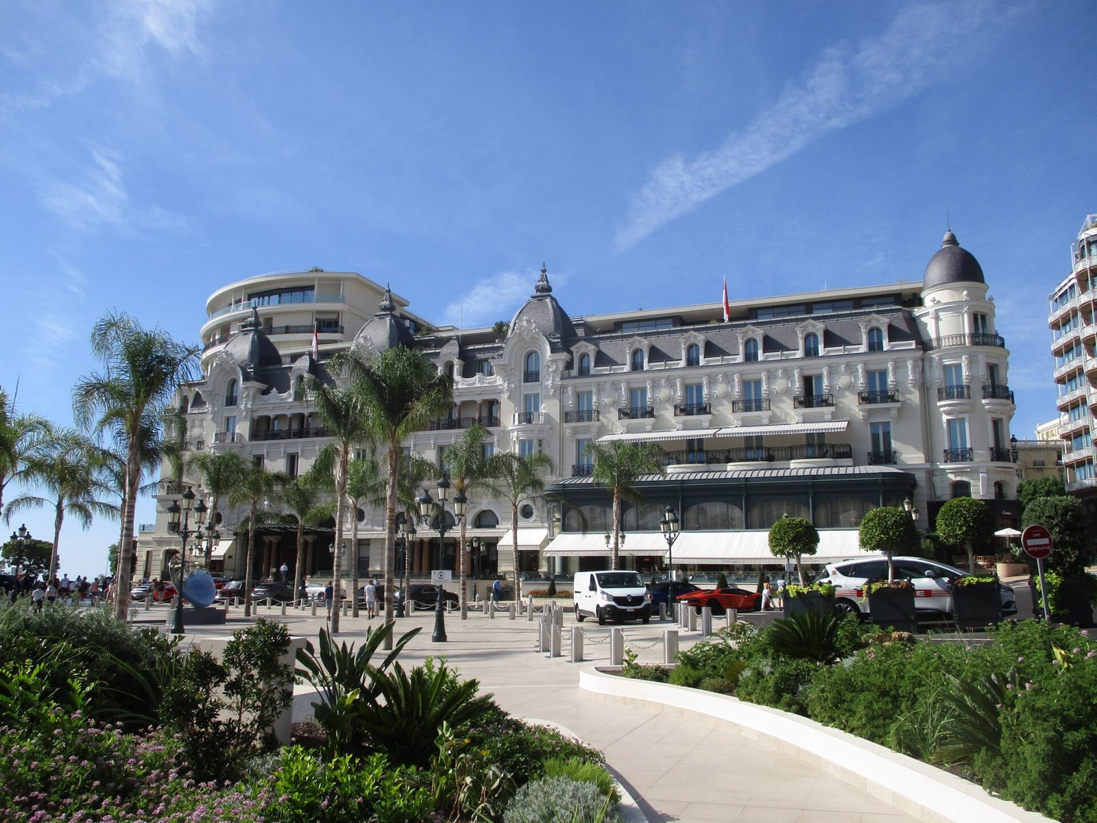Facade of the Hôtel de Paris in Monte-Carlo with palm trees and cars in front on a sunny day.