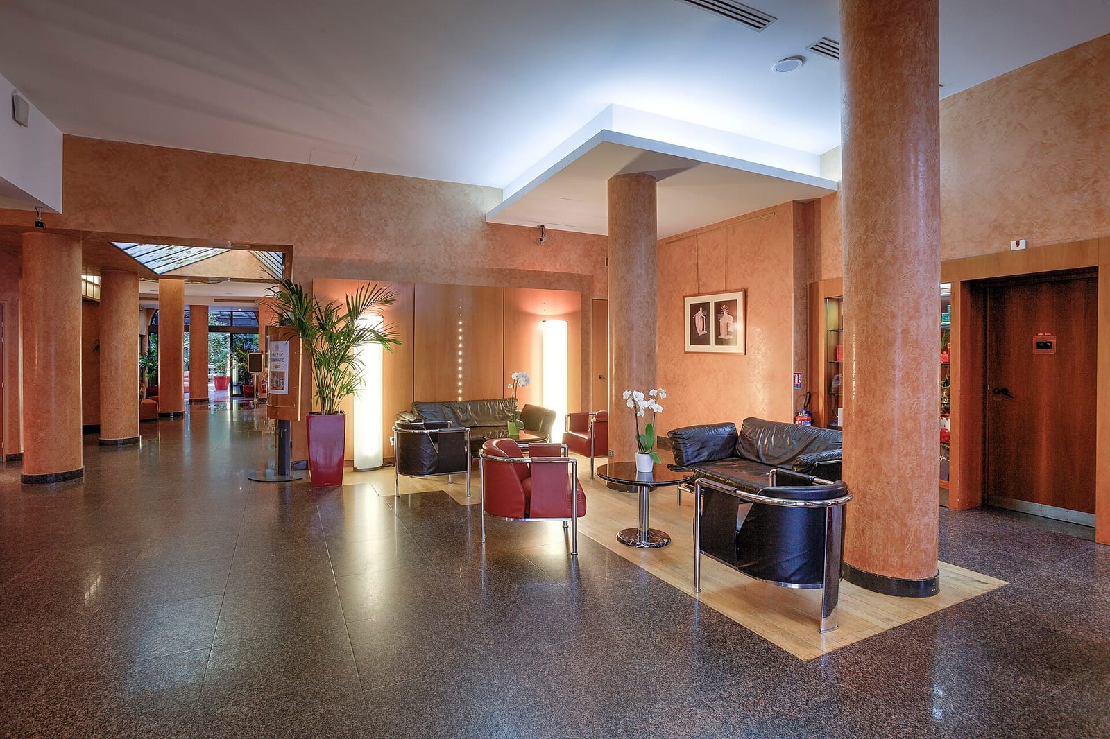 Lobby of a mid-scale Paris hotel with terracotta walls, dark leather seating and a small framed picture beside the lift.