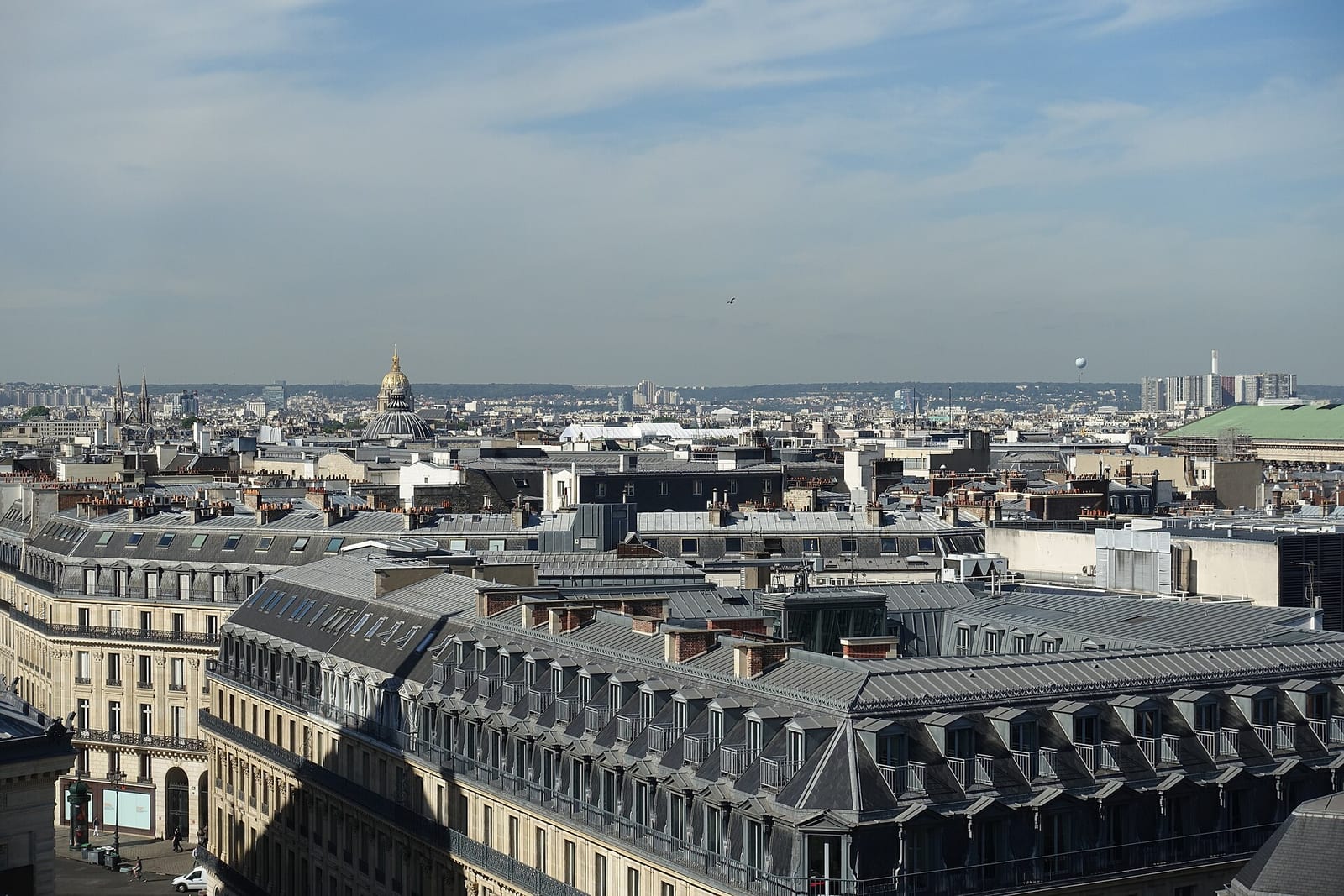 Zinc and slate rooftops of central Paris seen from a department-store terrace, the dome of Les Invalides on the horizon.
