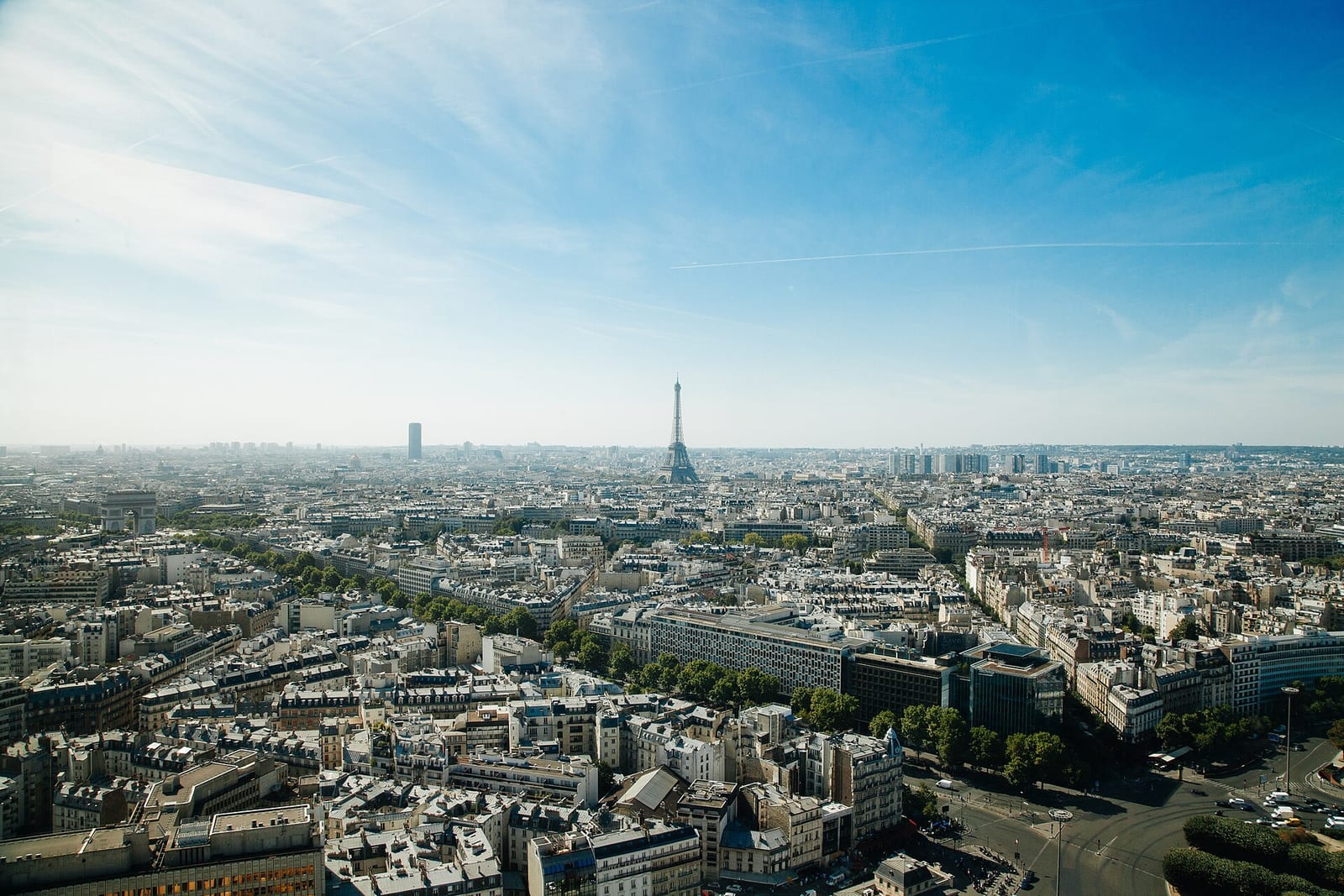 Aerial view over Paris from the west, Haussmann rooftops stretching to the Eiffel Tower under a clear sky.