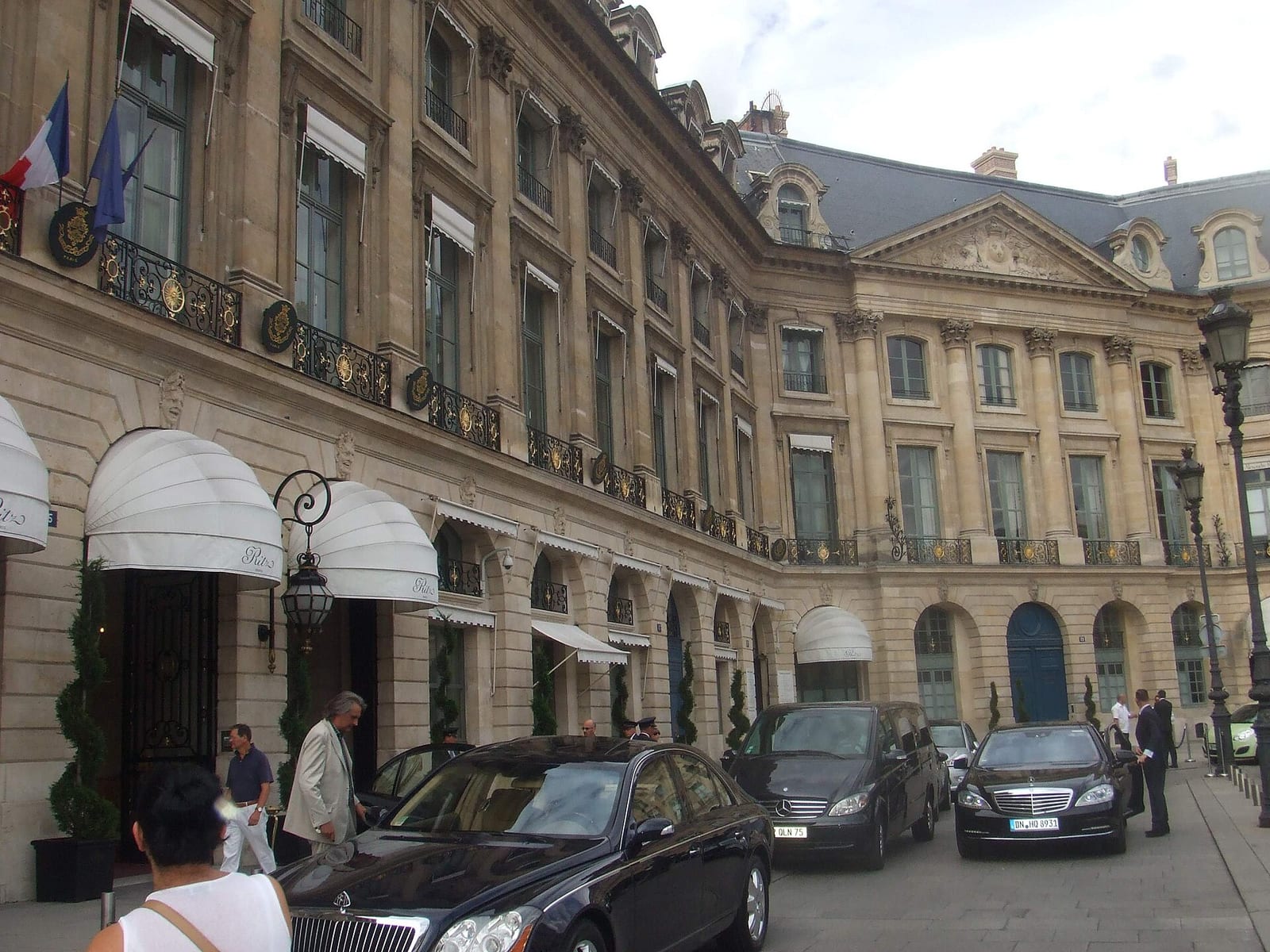 Facade of the Hôtel Ritz on Place Vendôme, Paris, with its awnings, lanterns and black cars at the entrance.