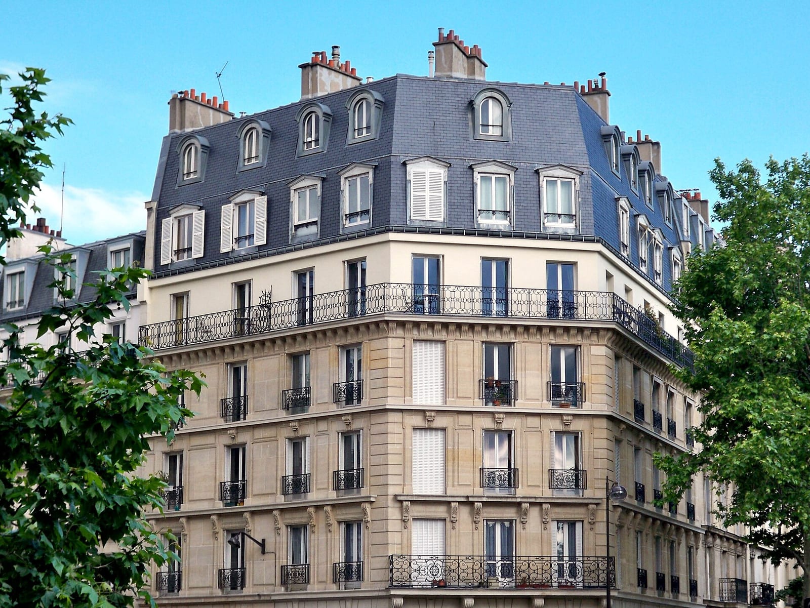 A cream-stone Haussmann apartment building in Paris with wrought-iron balconies, tall windows and a slate mansard roof.