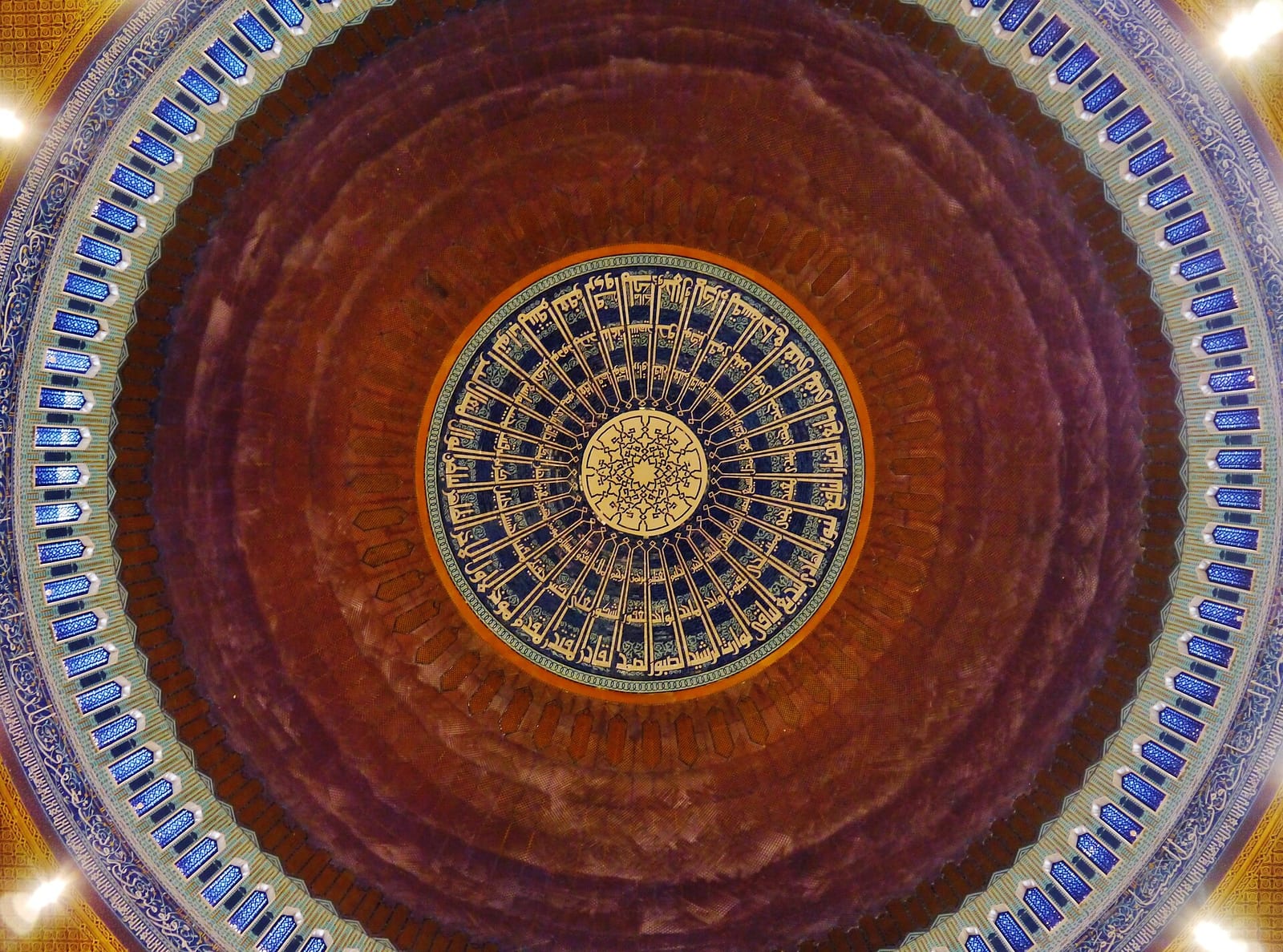 Looking up into the blue and gold dome of the Grand Mosque of Kuwait City with radiating geometric and floral ornament, December 2022.
