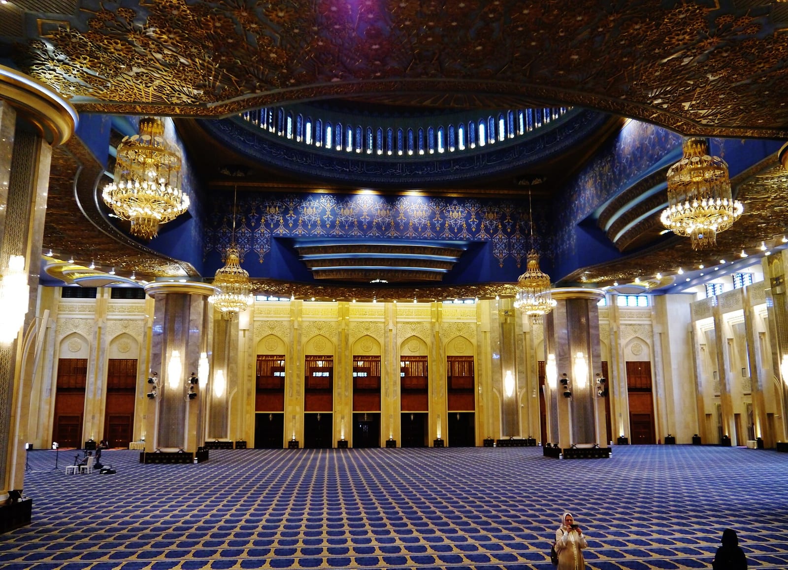 Interior of the Grand Mosque of Kuwait City with carved plaster, gilded calligraphy and rows of chandeliers beneath a high ceiling, December 2022.