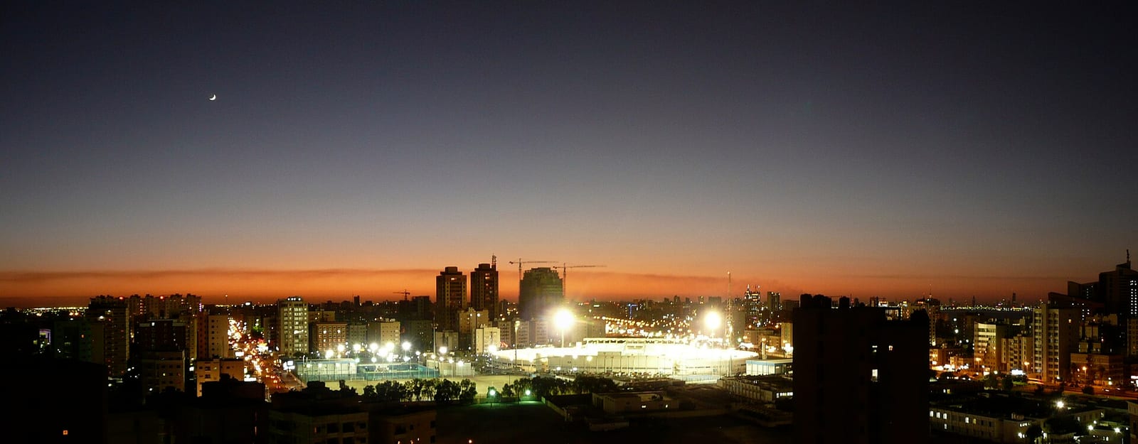 Stitched night panorama of Salmiya, Kuwait, taken from an apartment living-room balcony, showing lit mid-rise blocks and streets, December 2007.