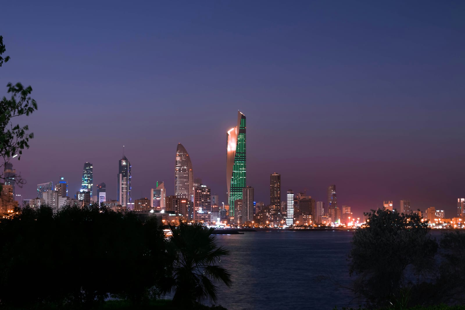 Kuwait City skyline lit at night, photographed from Green Island on Gulf Street with the towers reflected in the water.