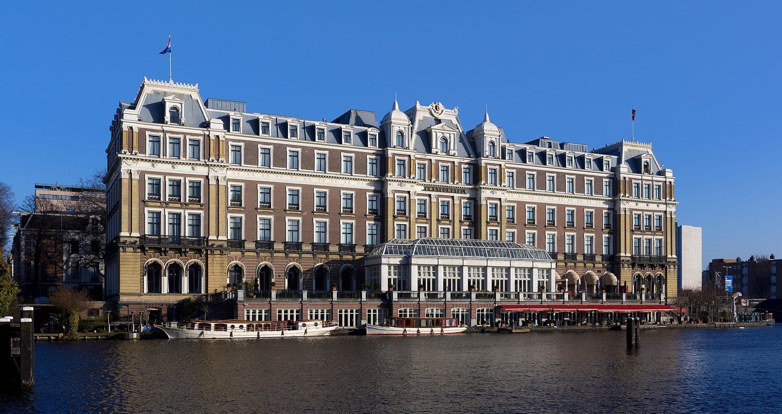 The InterContinental Amstel Hotel on the bank of the river Amstel in Amsterdam, with boats moored along the quay.
