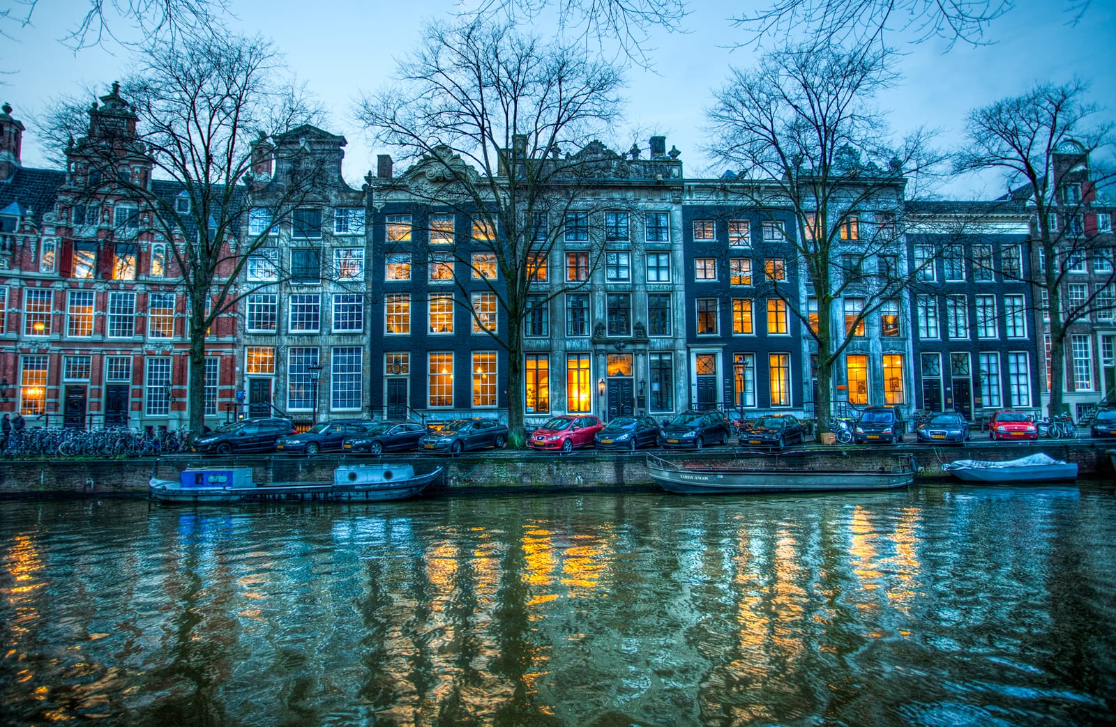 Tall, narrow 17th-century canal houses on the Herengracht in Amsterdam, lit from inside at dusk on a winter evening.