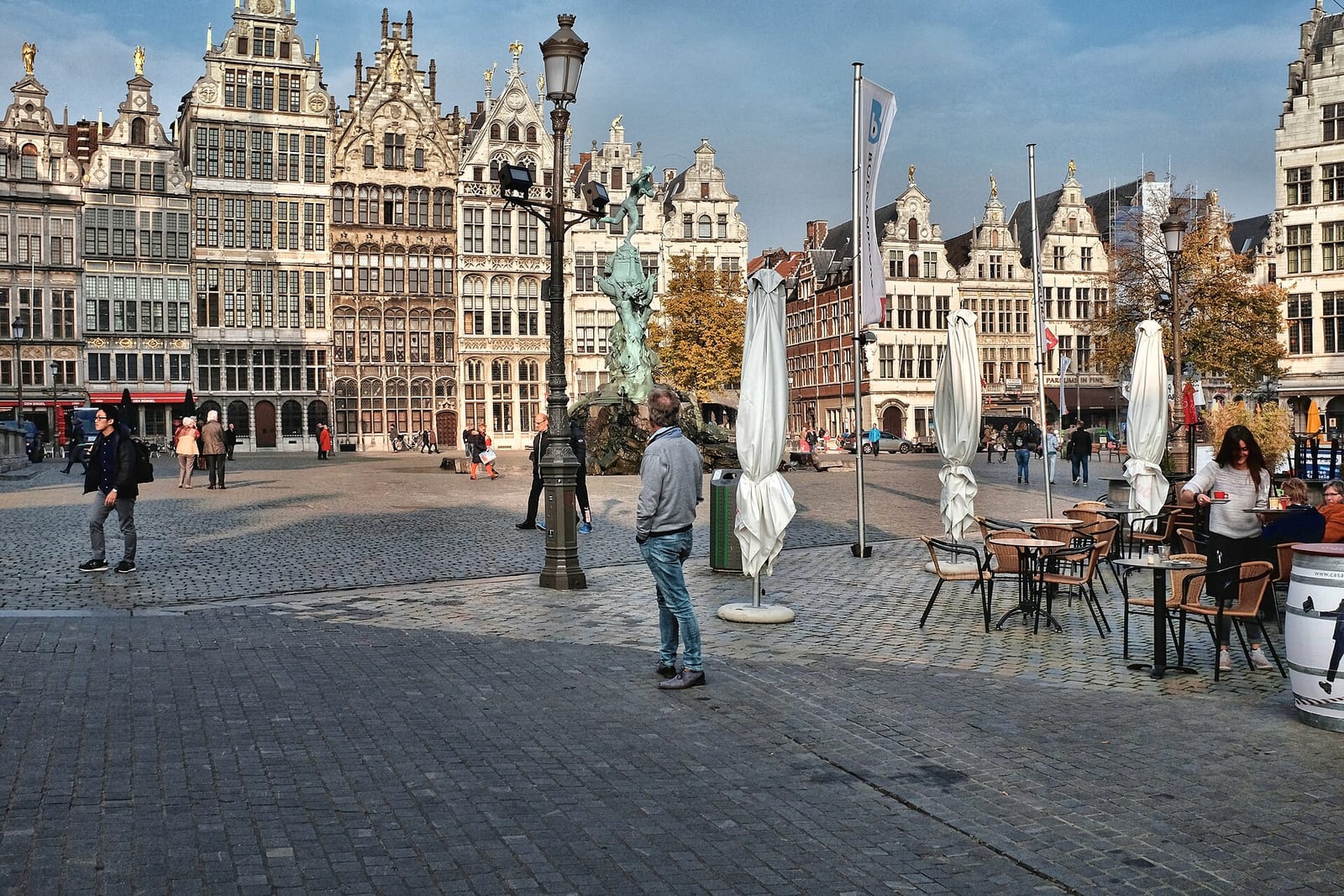 Stepped-gable guild houses and the Brabo fountain on the Grote Markt in Antwerp, with café tables in the square.