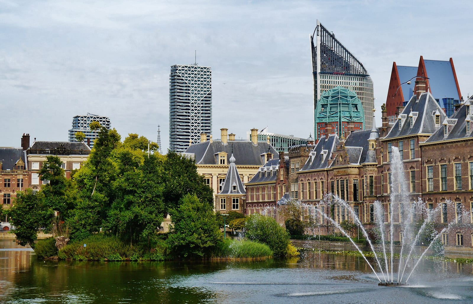 The historic Binnenhof parliament buildings on the Hofvijver pond in The Hague, with modern office towers rising behind them.