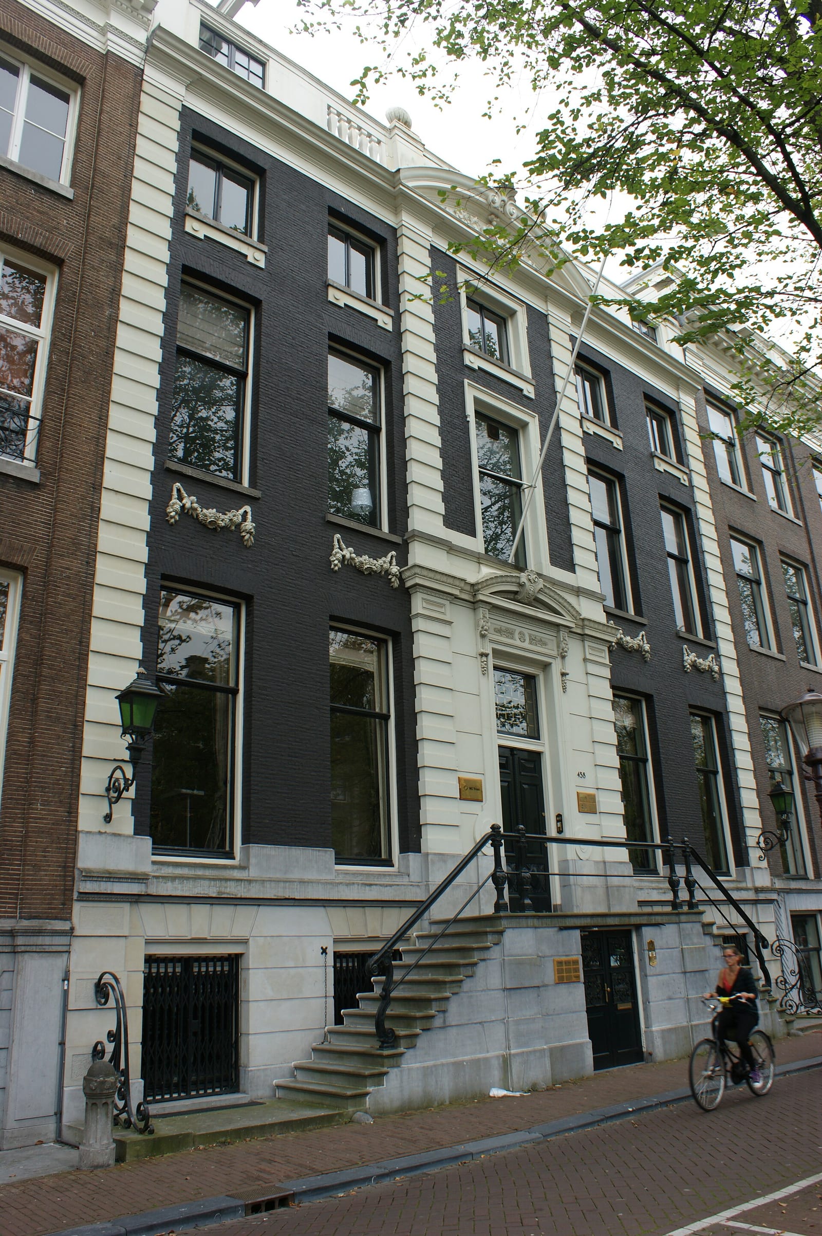 Street-level view of the stone-and-brick facade of Herengracht 458, a listed Amsterdam canal house with its raised bel-etage entrance.