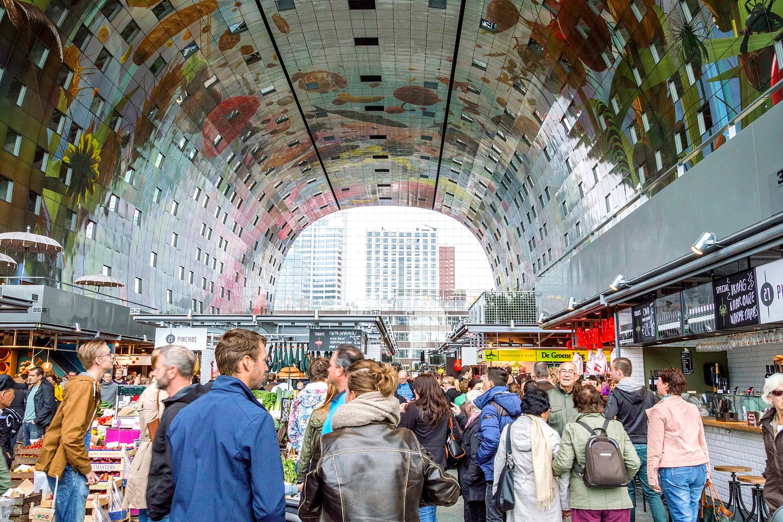 Crowds inside the Markthal in Rotterdam under its arched ceiling painted with a giant mural of fruit, vegetables and flowers.