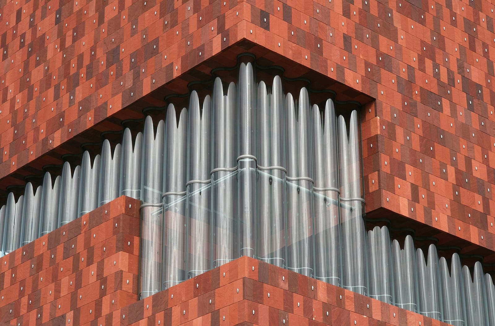 The red sandstone and curved glass facade of the MAS museum on the Antwerp docks, seen from below.