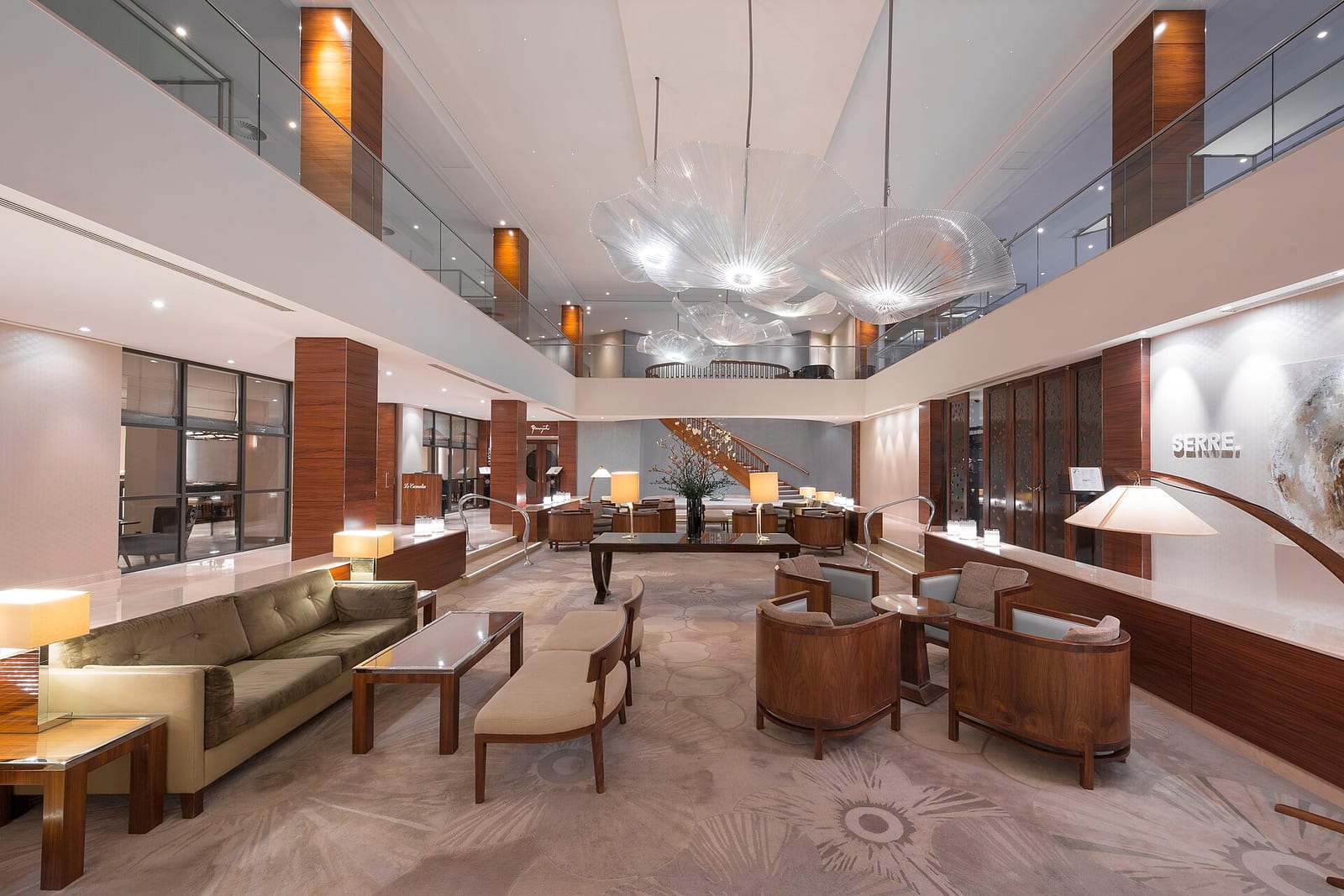 The lobby lounge of Hotel Okura Amsterdam with low seating, a long reception desk and a double-height ceiling.