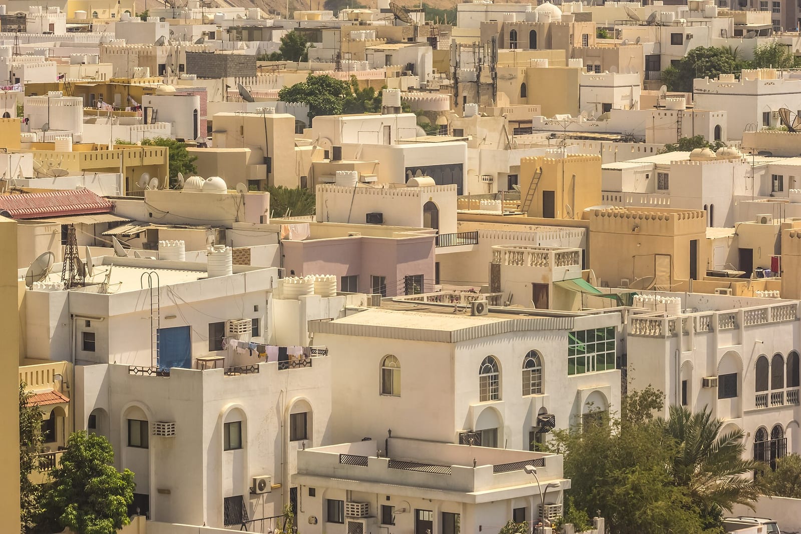 Dense cluster of two- and three-storey white villas with arched windows and parapets in Al Khuwair, Muscat.