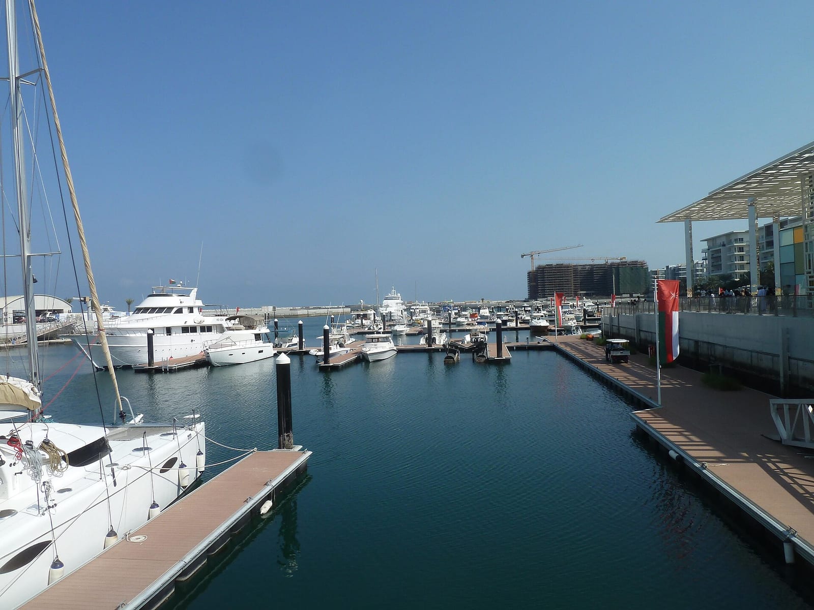 Yachts moored at the Al Mouj marina in Muscat with contemporary white residential buildings and a hotel tower behind.