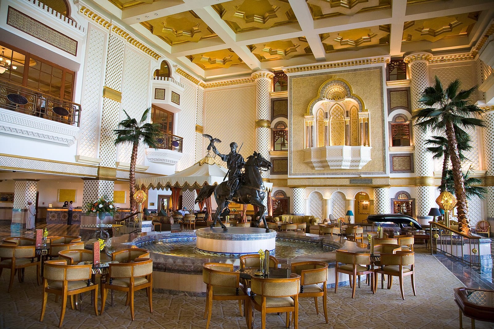 Ornate lobby of the Grand Hyatt Muscat with a bronze equestrian sculpture, palm trees, gilded ceiling and stained glass.