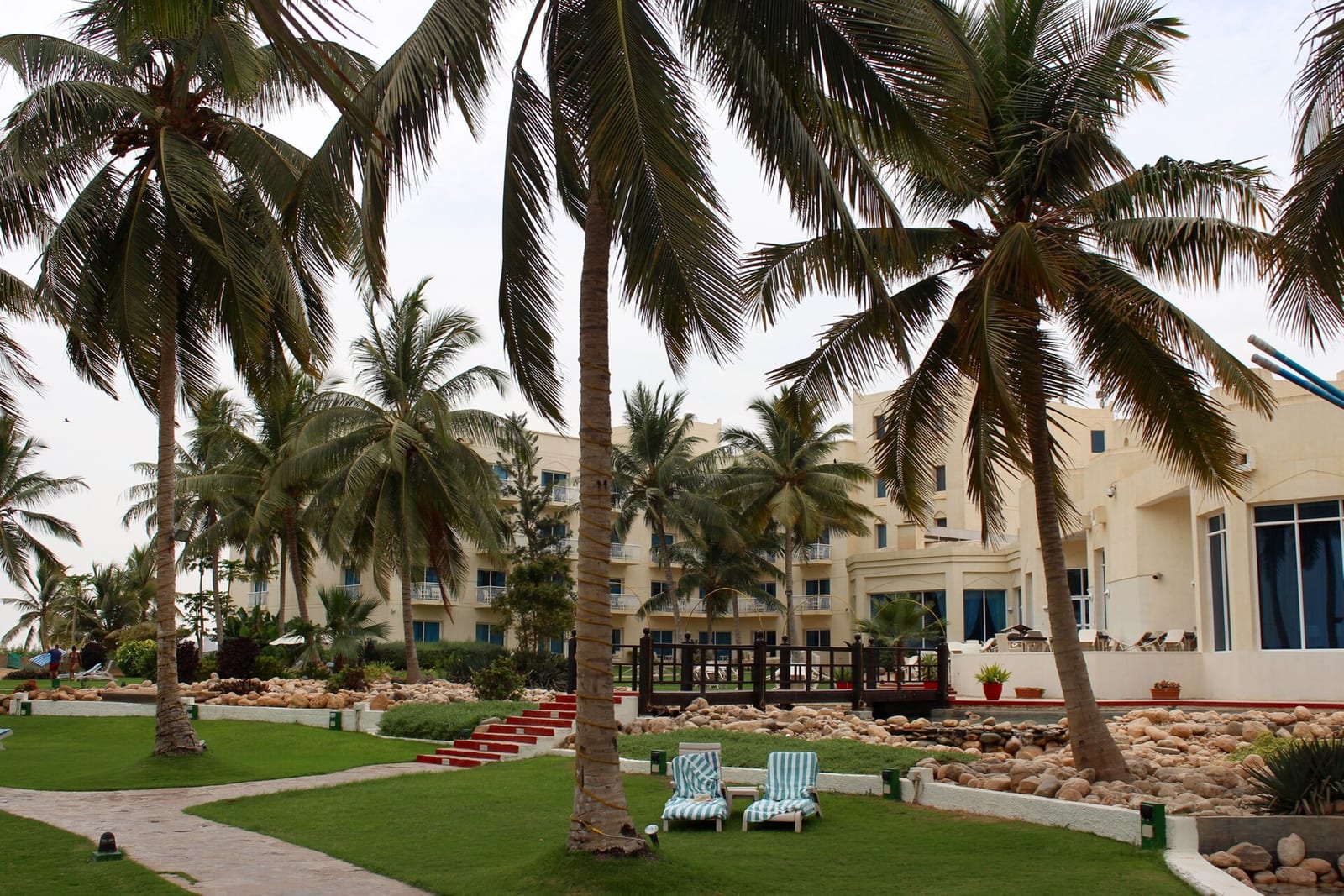 Low white buildings of the Hilton Salalah resort among tall coconut palms and lawns in Dhofar.