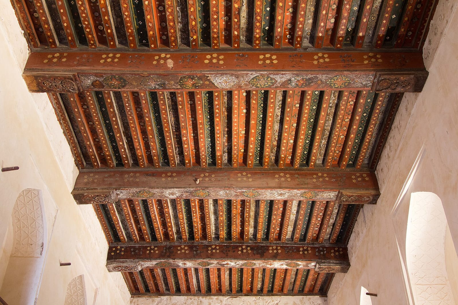 Painted wooden ceiling beams in red, black and ochre with floral and geometric motifs at Jabrin Castle, Oman.