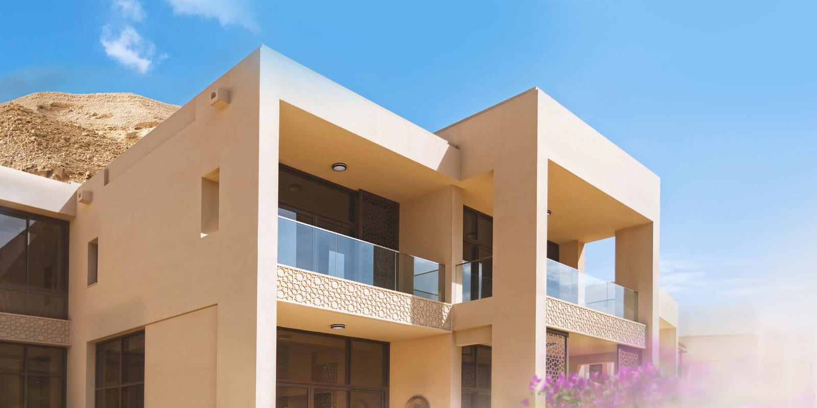 Contemporary stone-clad hilltop villas with flat roofs and glass balconies at Muscat Bay, photographed for a property listing.