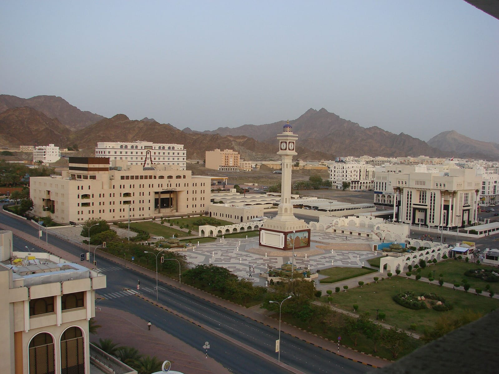 Low-rise office blocks, a mosque minaret and landscaped roads in Ruwi, Muscat's central business district, with hills behind.