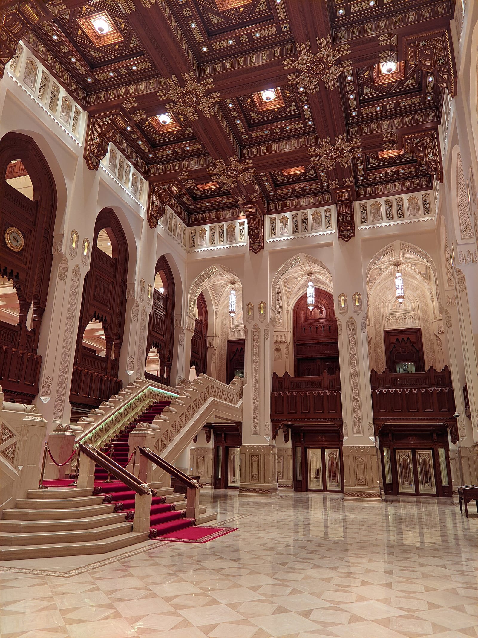 Tall pointed arches, carved wood screens and stone columns rising through a double-height gallery at the Royal Opera House Muscat.