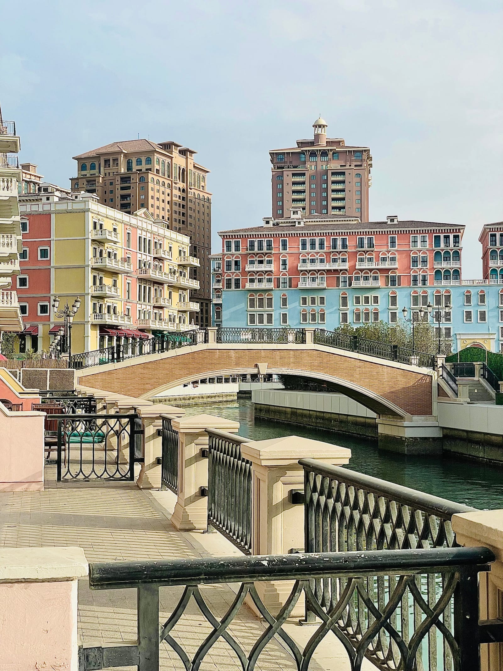 Pastel yellow, coral and blue canal-side apartment blocks and a footbridge in the Qanat Quartier of The Pearl-Qatar.