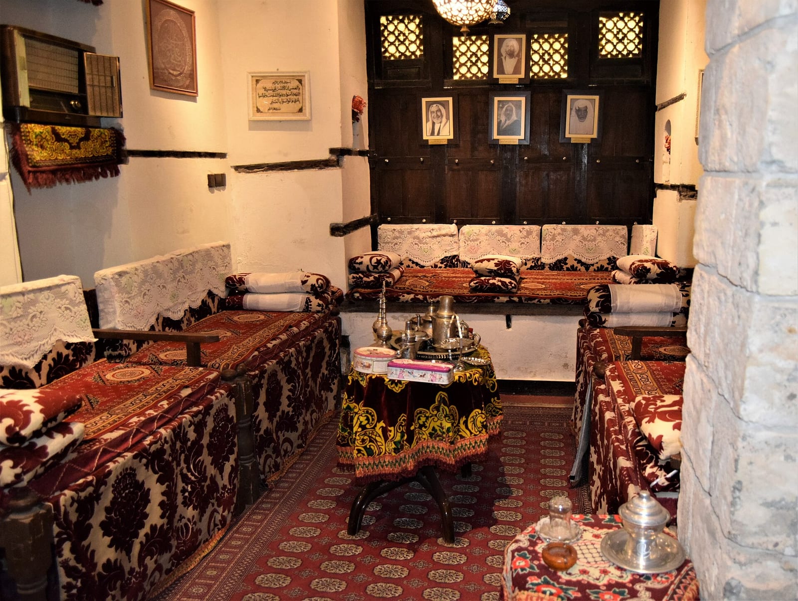 Traditional Hejazi reception room in Historic Jeddah with bench seating along the walls, patterned textiles and framed pictures.