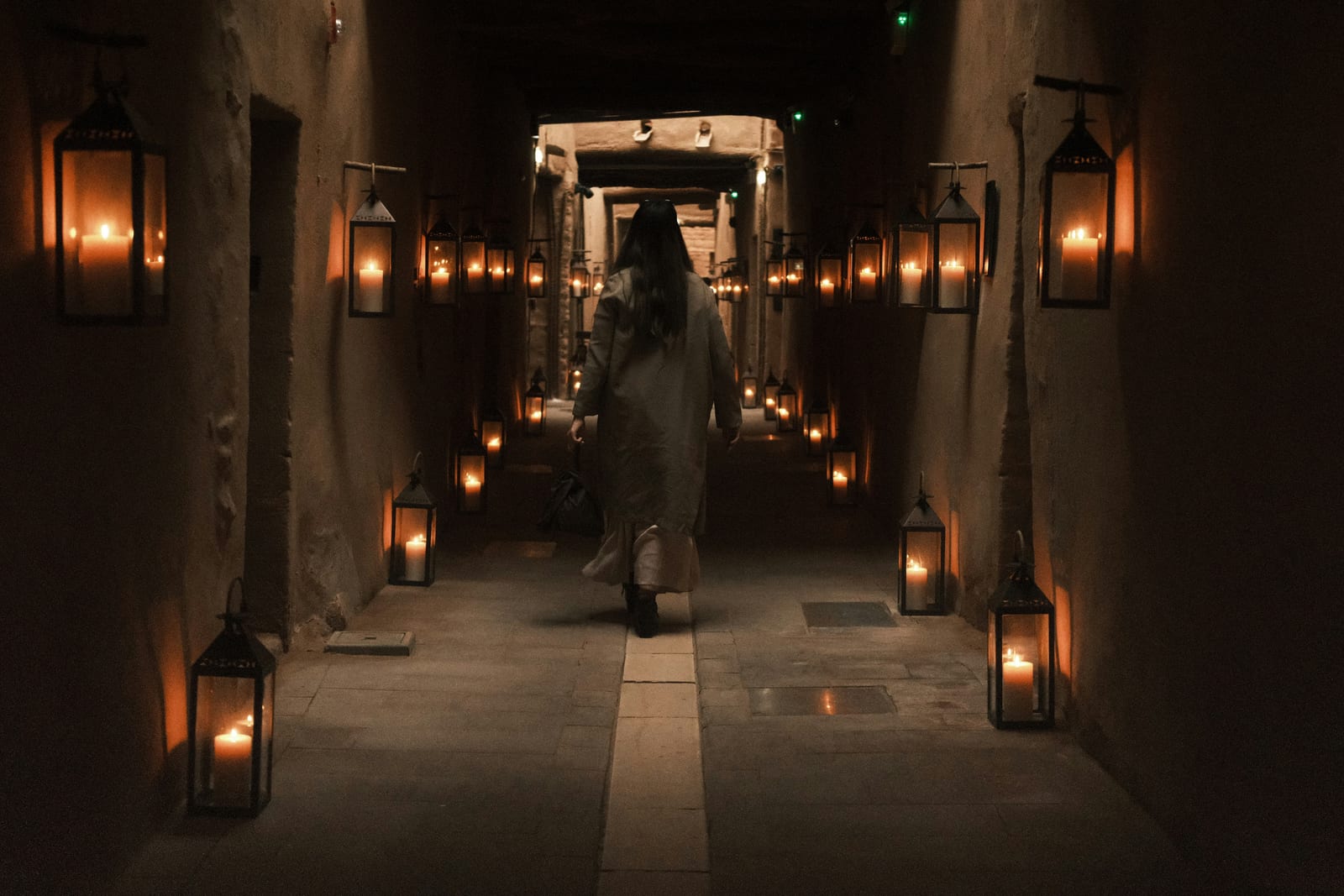 Lantern-lit mud-brick hallway inside the Dar Tantora hotel in AlUla Old Town with a guest walking through, 2026.